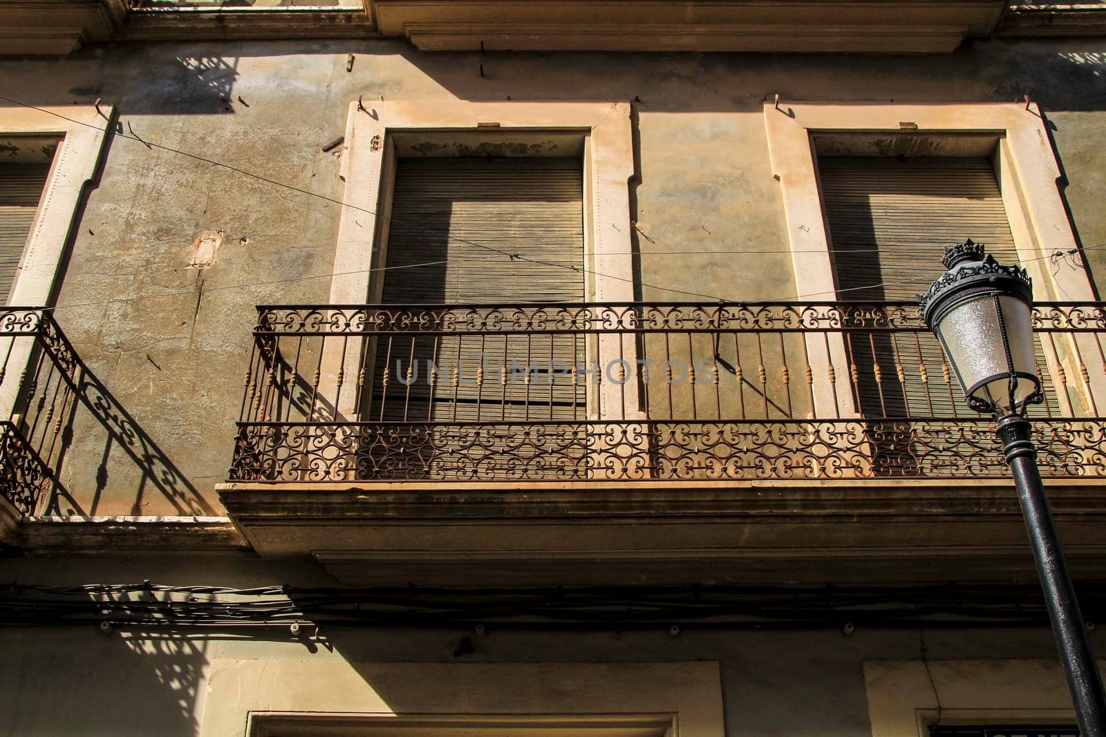 Old house facade with rusty balcony and blind next to vintage streetlight. Novelda village, Valencia community, Spain.