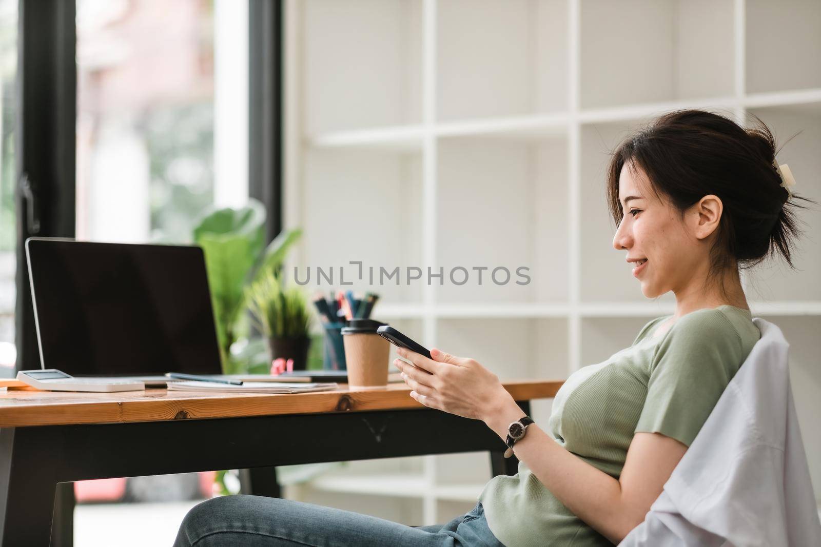 Happy asian woman using mobile phone at modern office,