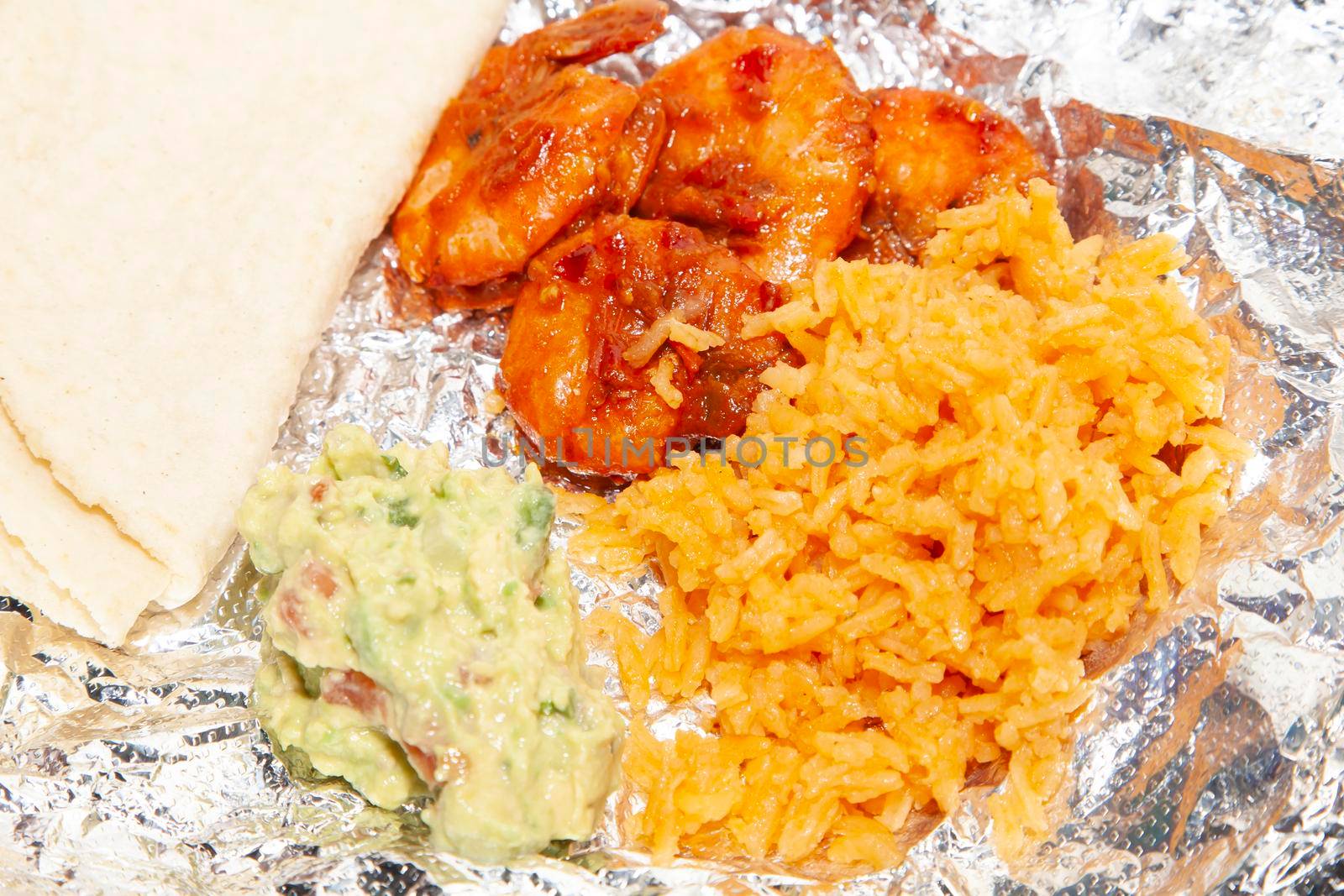 Spicy hot shrimp on foil next to folded corn tortillas, rice, and guacamole
