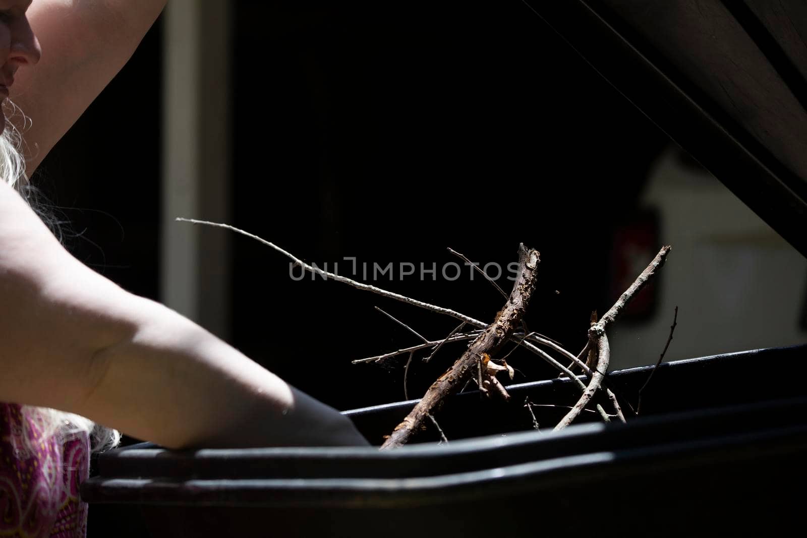 Woman reaching in to put sticks in a garbage can