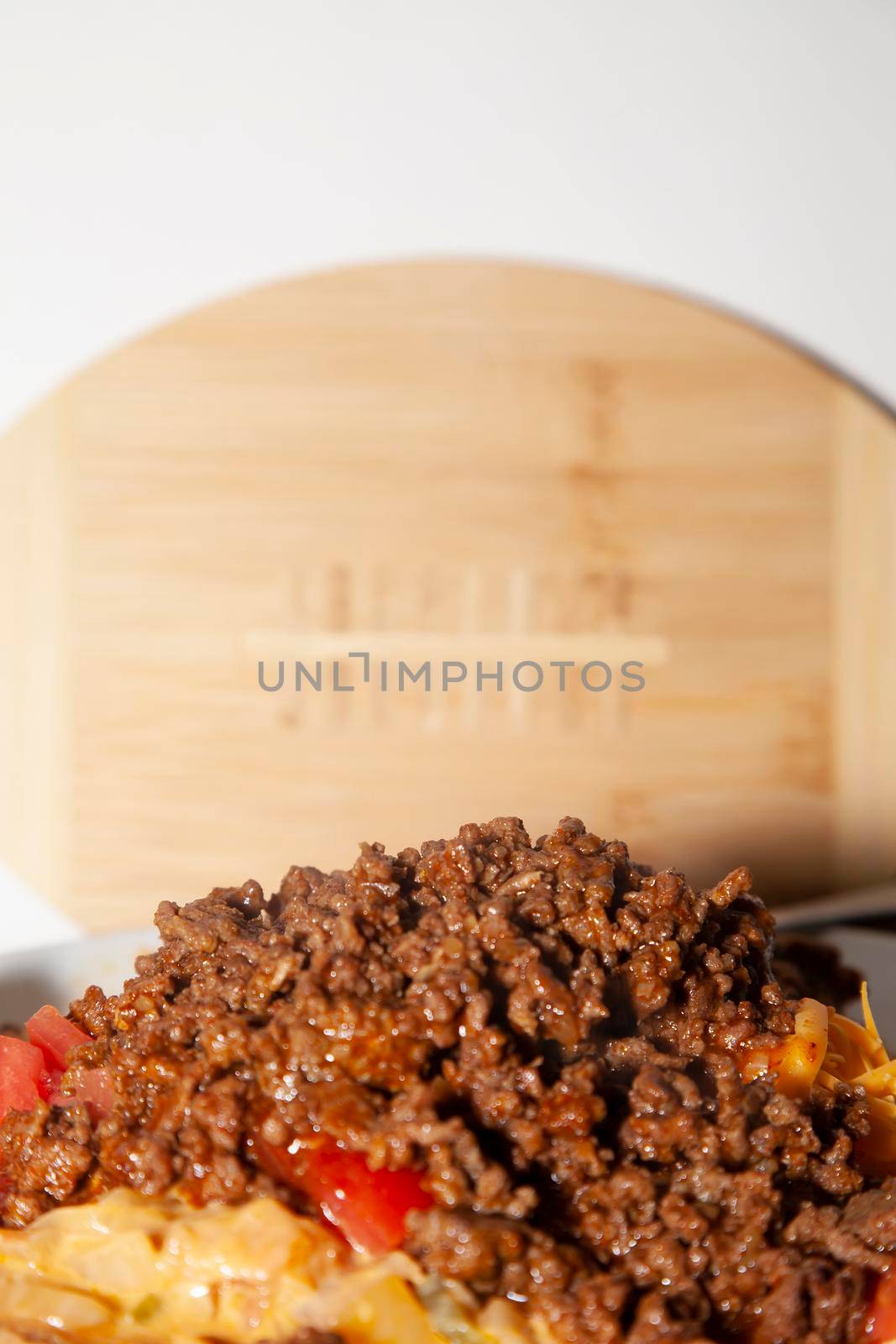 Spicy ground beef on a white plate with diced tomatoes and shredded cheese in front of a wooden football