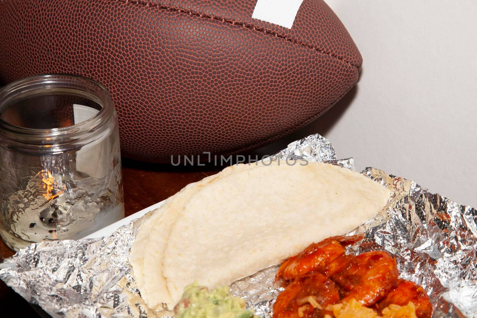 Spicy hot shrimp on foil next to folded corn tortillas wih a candle and a football in the background
