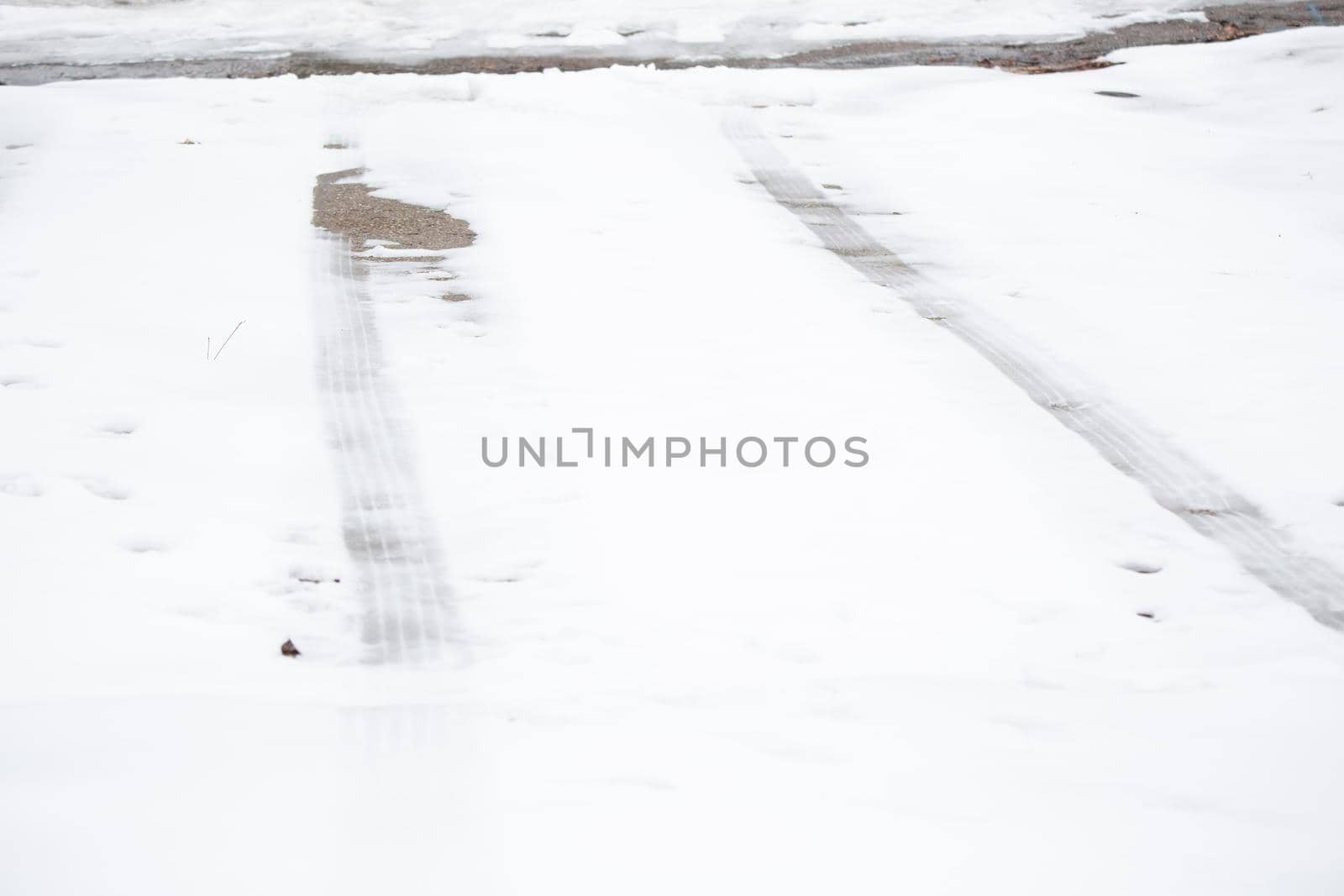 Tire tracks on a dangerously slick driveway covered in winter precipitation