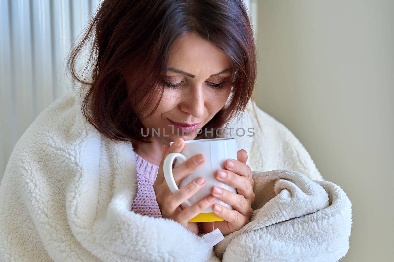 Heating during the cold winter autumn season. An adult woman warming herself with a blanket, a central heating radiator, hot tea.