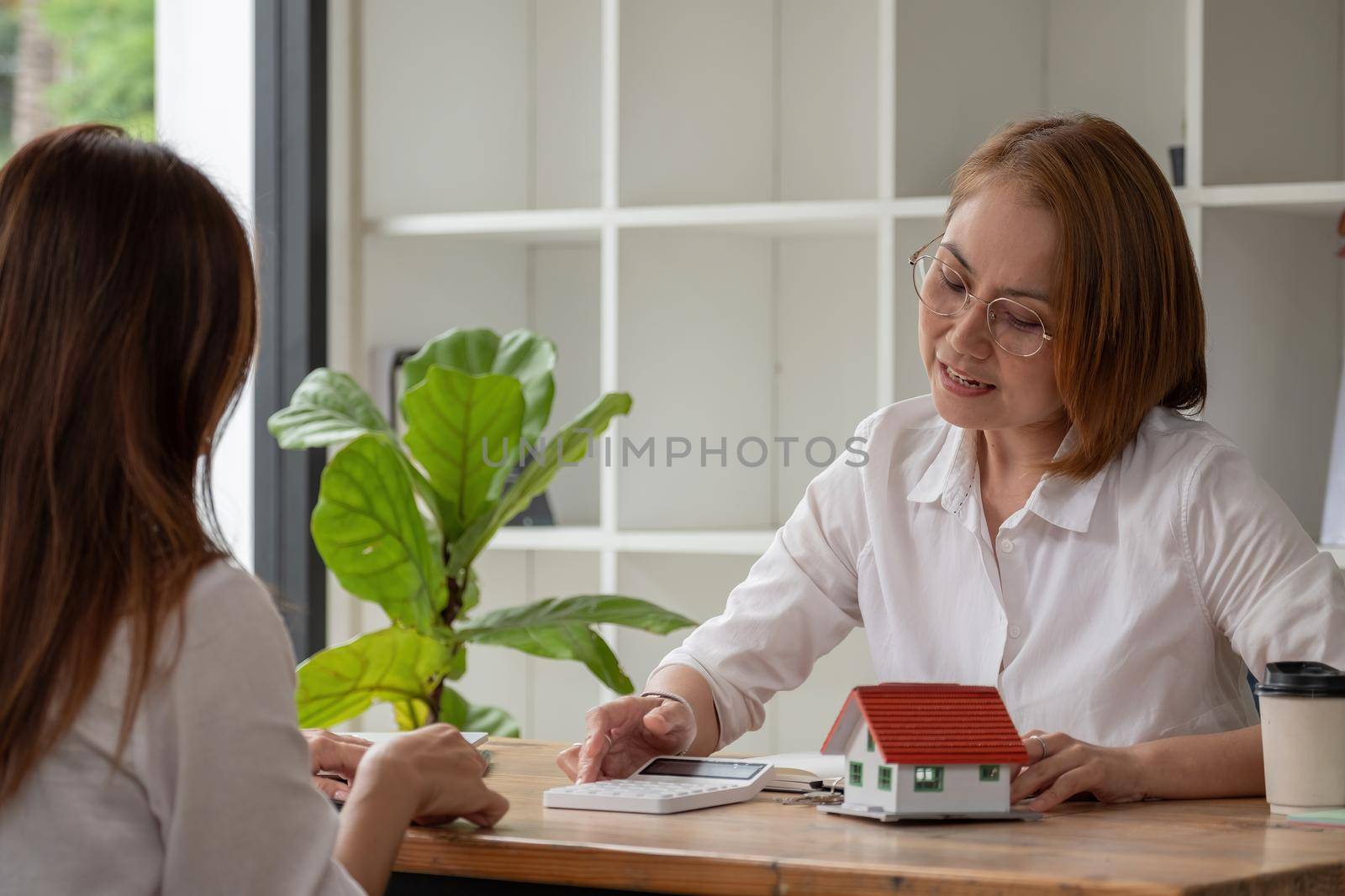 Real estate broker agent being analysis and making the decision a home estate loan to customer, She using calculator to presentation detail and waiting for her reply to finish by nateemee
