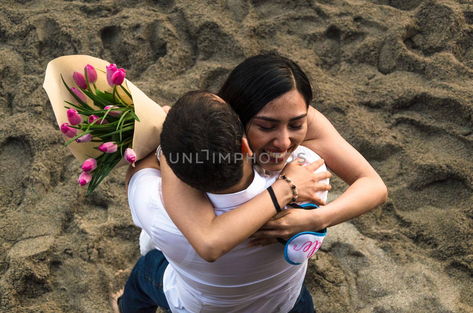 Young couple in love, with a bouquet of tulips cuddling on the beach at sunset