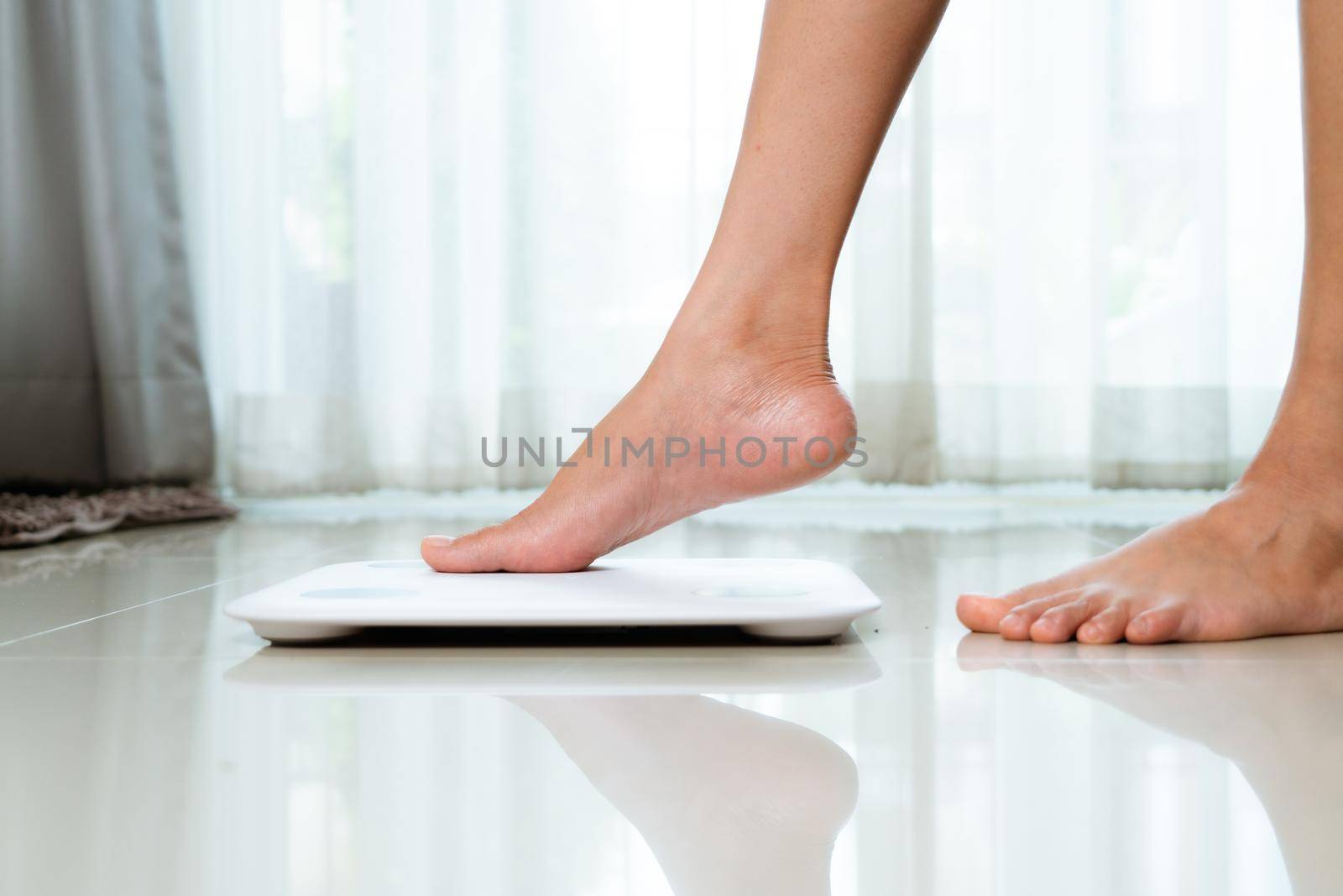 Female leg is stepping on white scales at home