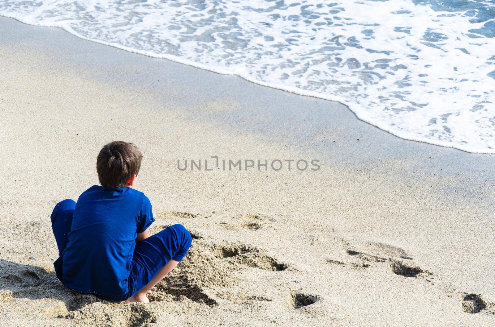 A boy looking at the sea with his back to the camera. Child looking at the sea on the beach