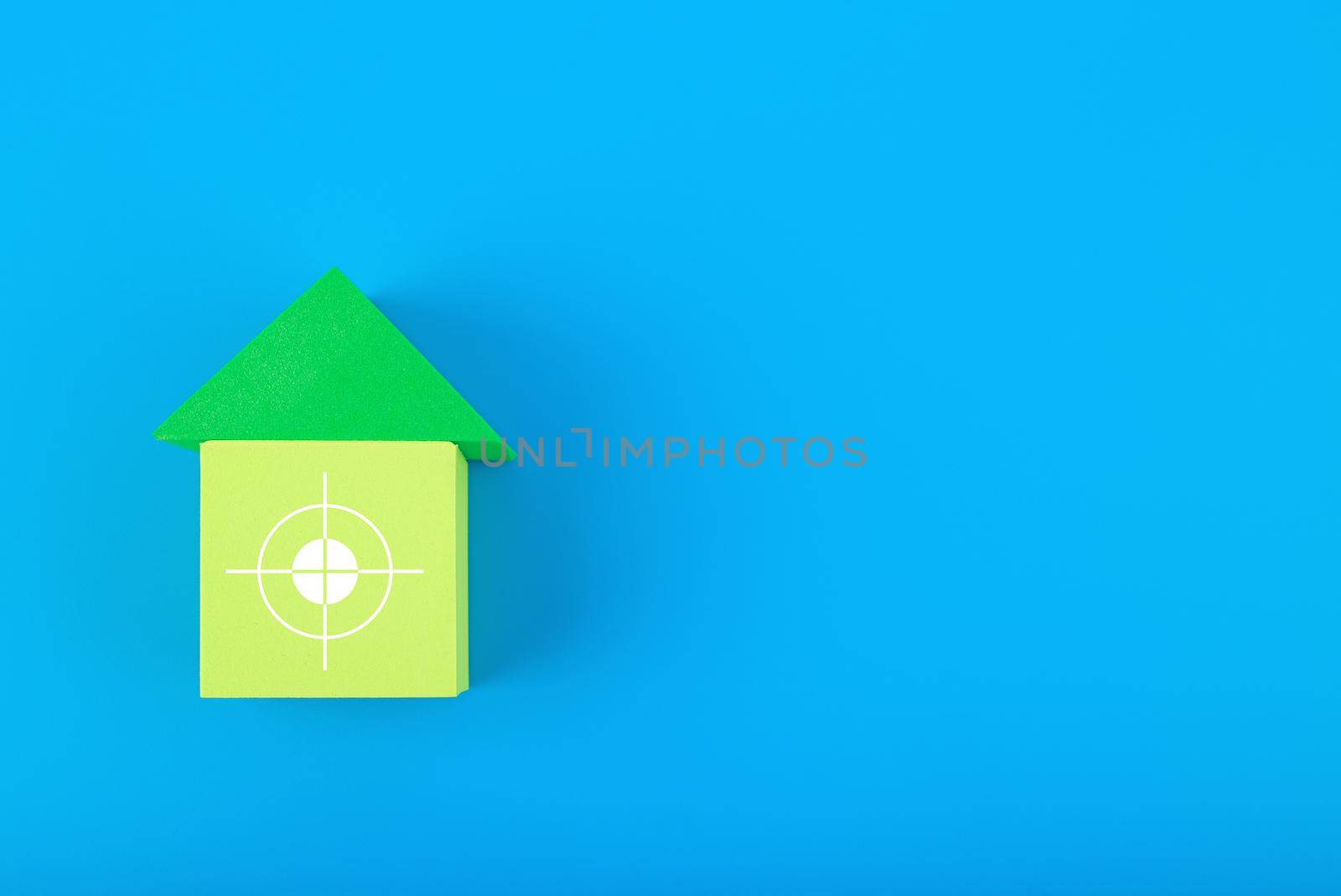 Mortgage, loan or saving money for home and investing in real estate trendy concept. Green toy house with white target in the middle against blue background with copy space