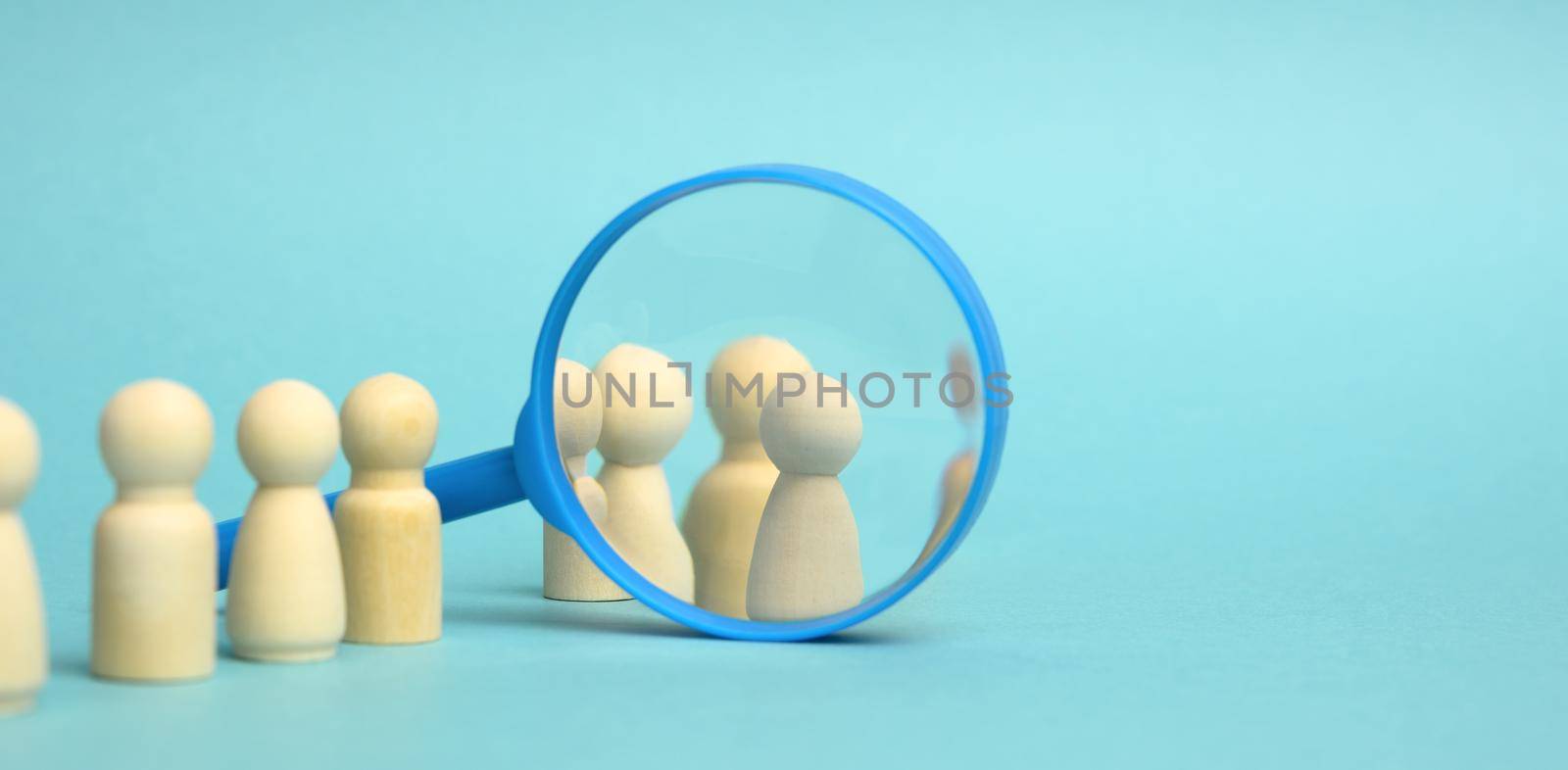 wooden figures of men stand on a blue background and a plastic magnifying glass. Recruitment concept, search for talented and capable employees, career growth, copy space
