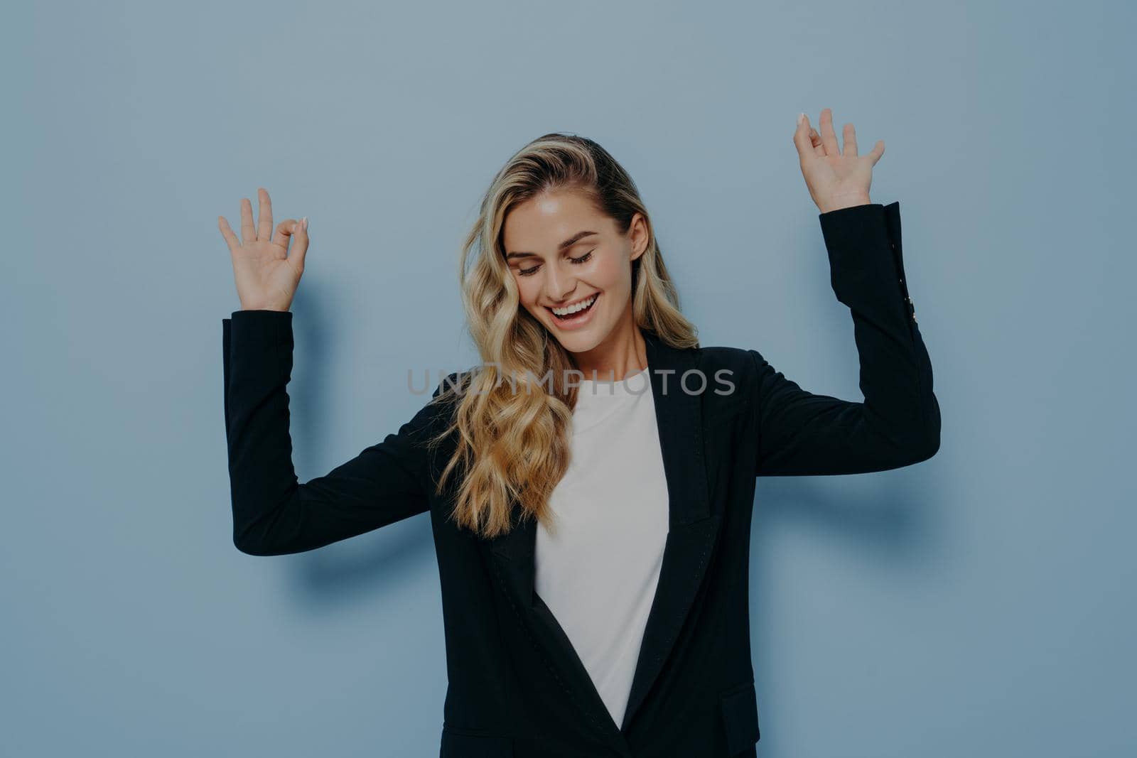 Carefree happy woman with blonde dyed hair raising her arms and dancing with closed eyes and smile on face by vkstock