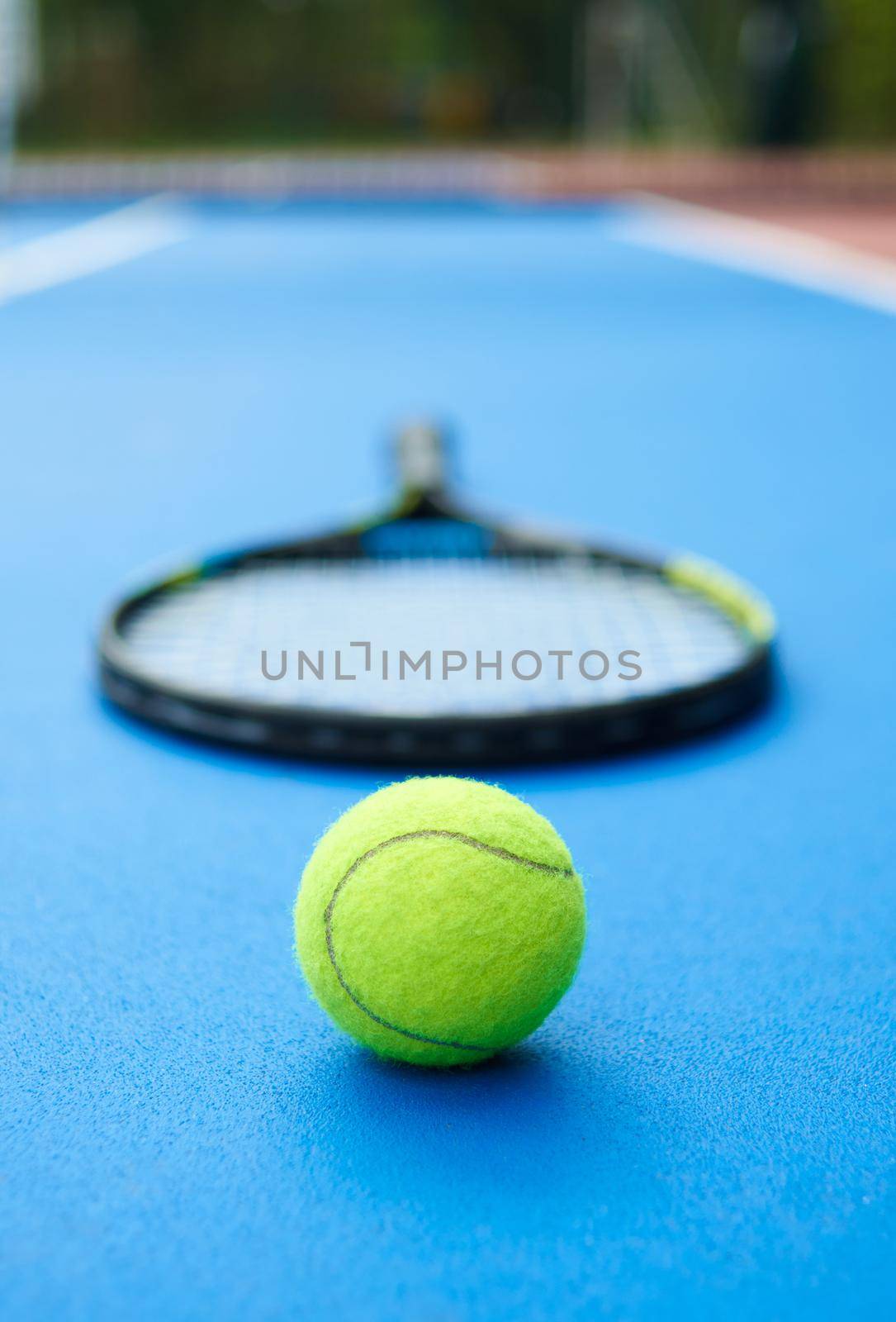 Yellow ball is laying on professional tennis racket background. A ball is on blue bright tennis cort carpet. Photo made in contrast saturated colors. Concept of sport equipment photo.