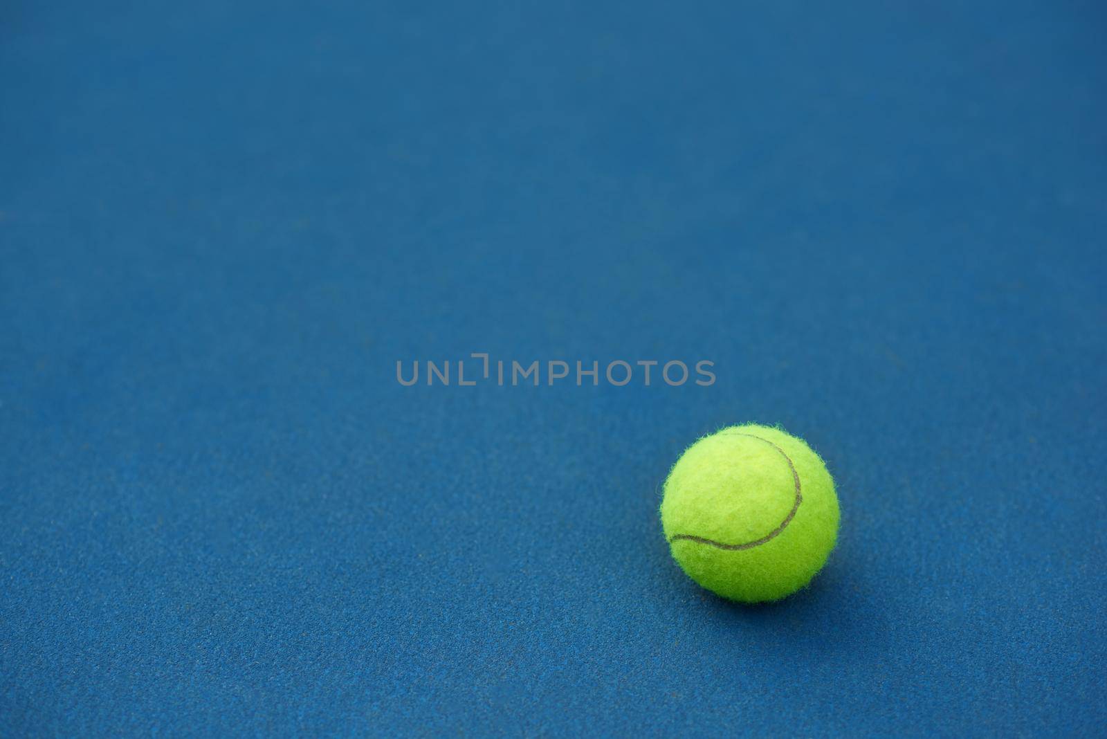 Yellow bright tennis ball is lying on on blue carpet. Made for playing tennis. Contrast image with satureted colors. Blue tennis court.