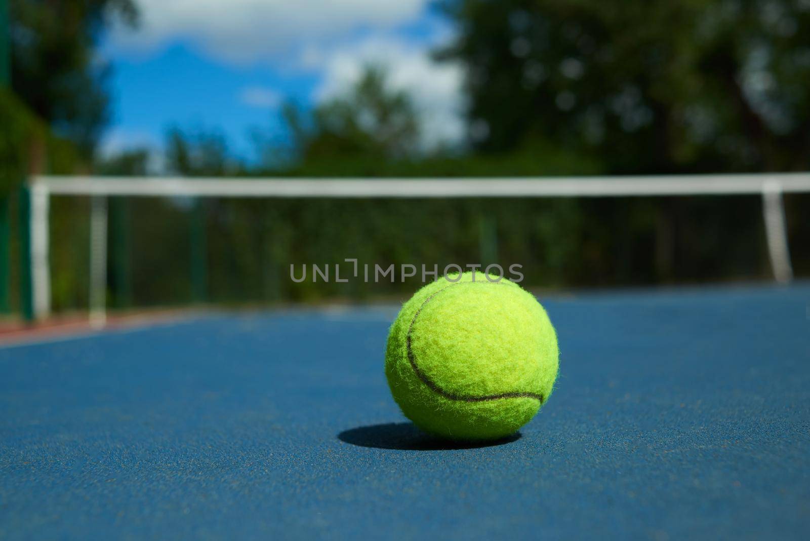 Frontview of bright tennis ball on blue carpet of opened court. by SerhiiBobyk