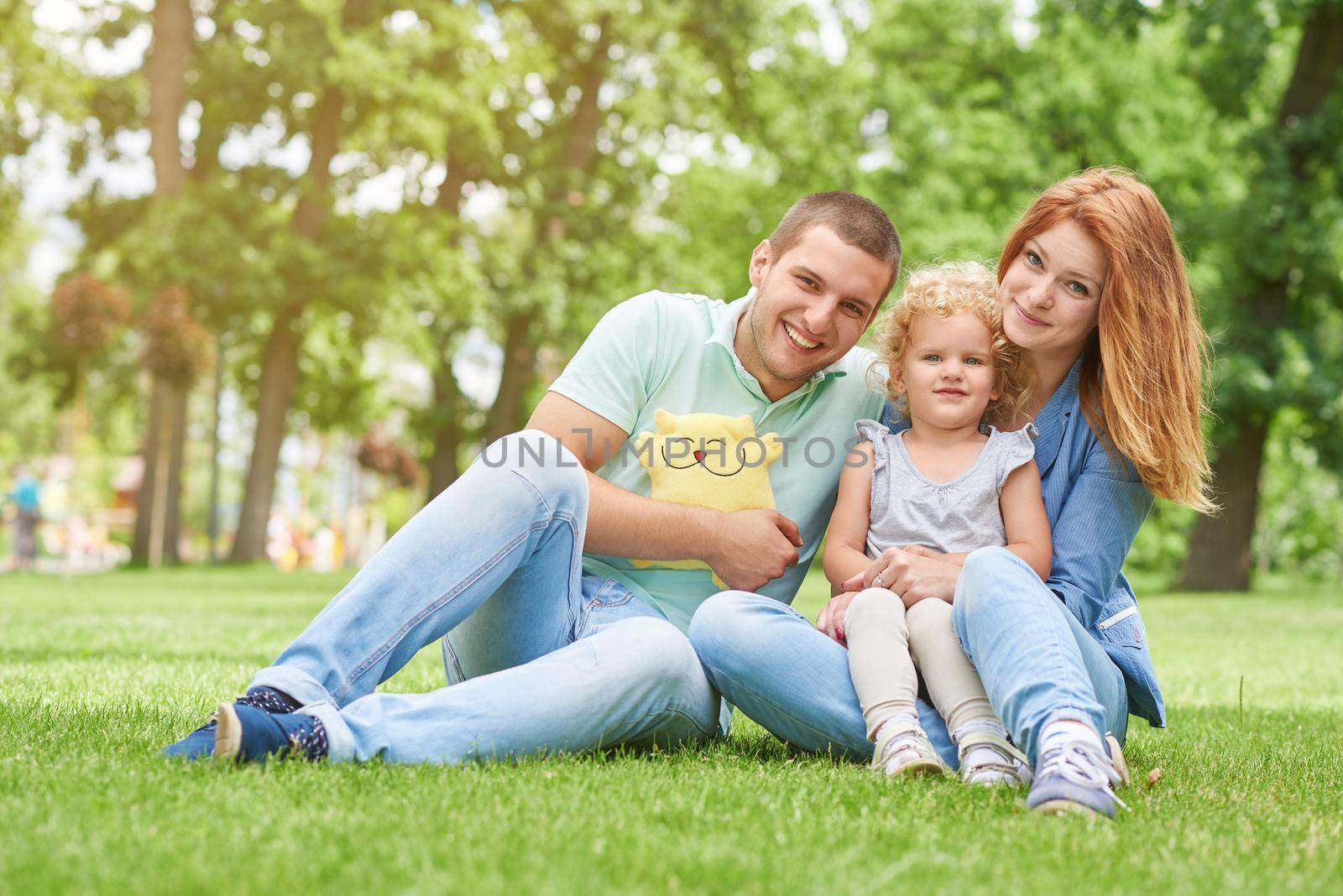 Young beautiful woman sitting on the grass with her happy husband and adorable little daughter copyspace love family marriage lifestyle seasonal enjoyment relaxing recreational concept.