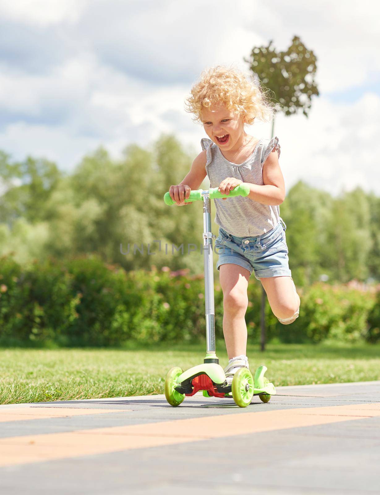 Vertical shot of a happy little girl laughing joyfully while riding kick-scooter at the park on a warm sunny day copyspace emotions expressive kids children happiness concept.