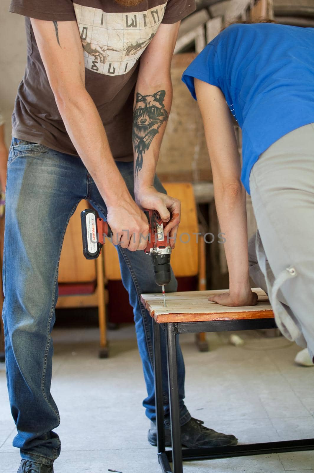 13.08.2021 - Ukraine, Goshcha, group of young workers is using power screwdriver drilling, hambler during construction wooden bench, do it together by balinska_lv