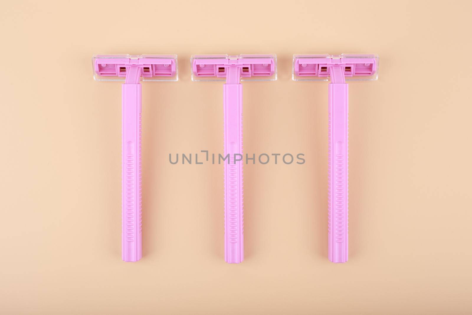 Top view of three pink razors in a row on light beige background. Concept of smooth skin, shaving and epilation