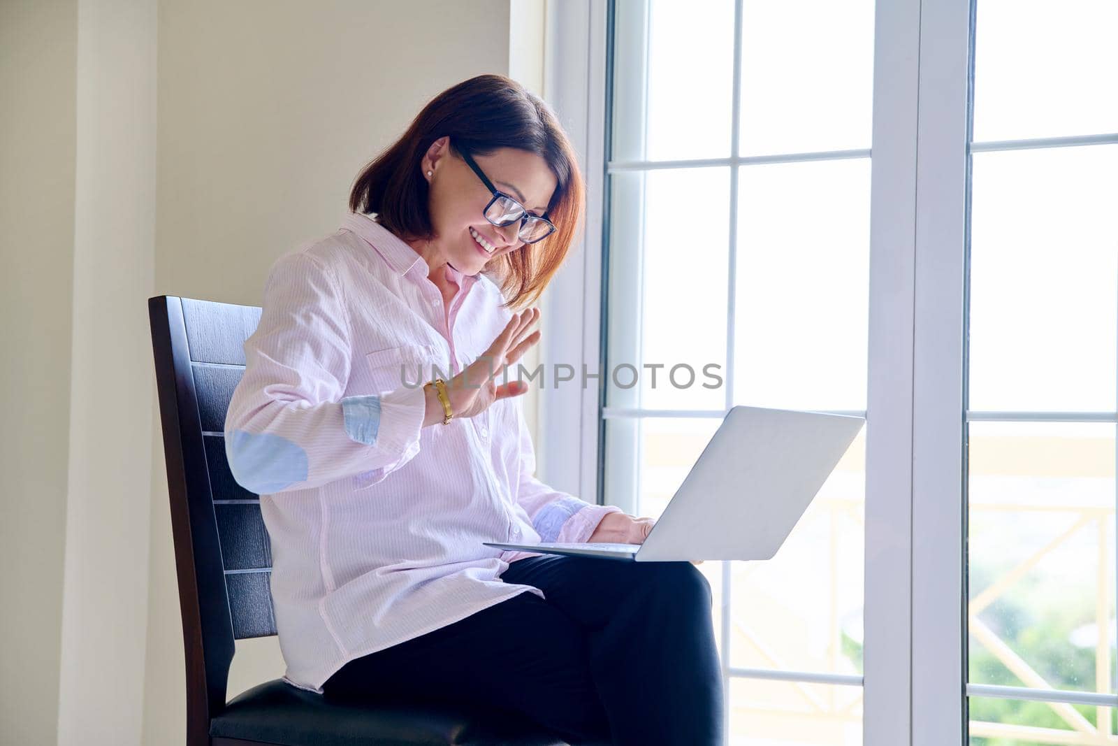 Video call, teleconference, online video meeting. Mature confident businesswoman, therapist, counselor, teacher, mentor sitting with laptop, looking at screen, talking, consulting working remotely