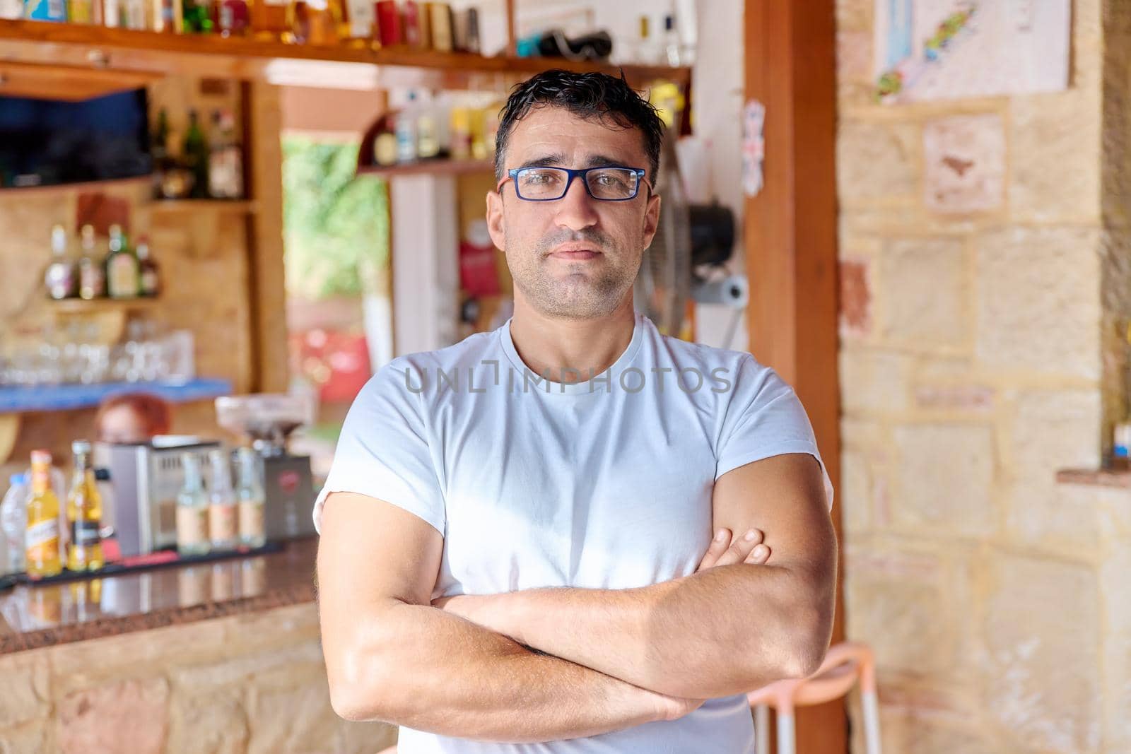 Portrait of positive confident middle aged man wearing glasses with crossed arms. Smiling male cafe bar owner looking at the camera. Small business, 40 people, concept ownership