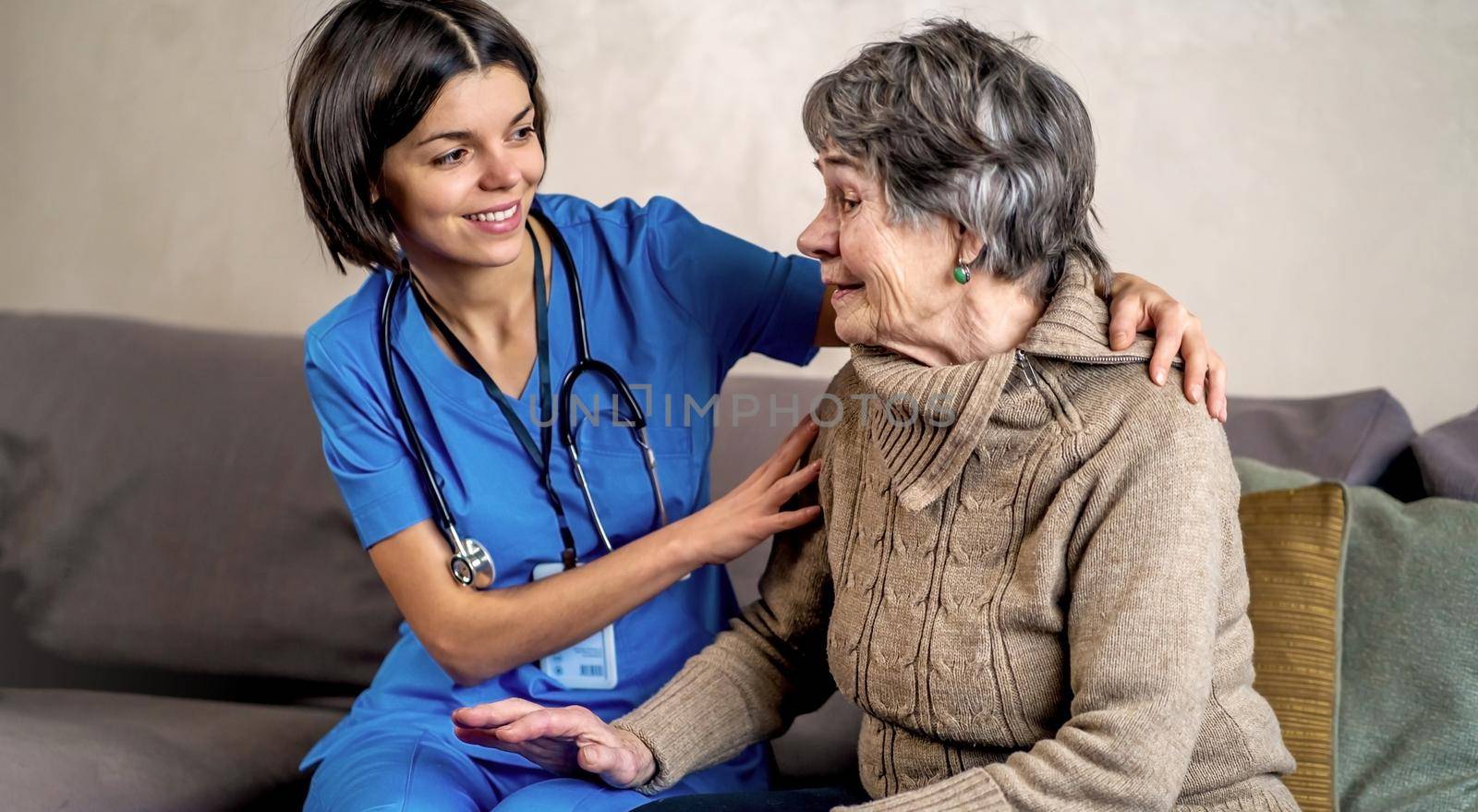 A young nurse takes care of an elderly 80-year-old woman at home, holds her hands . Happy retired woman and trust between doctor and patient. Medicine and healthcare.