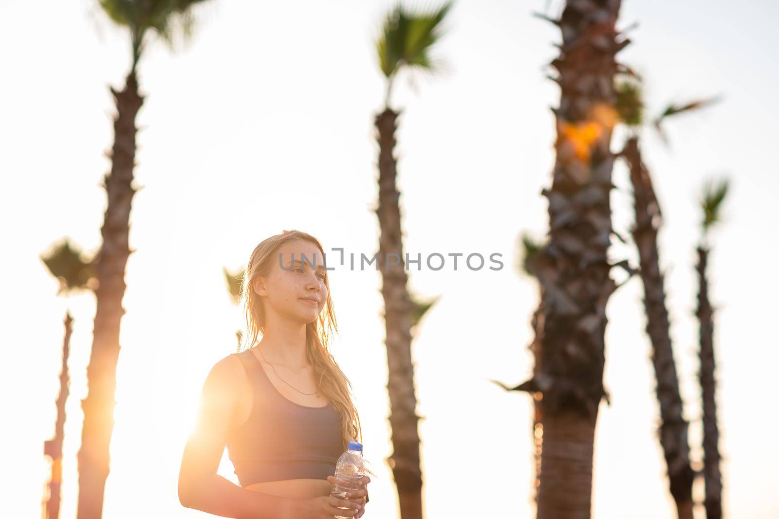 Young girl exercising on seafront line at sunset sunrise. Beautiful girl drinking water while jogging on sea promenade during summer Vacation Meditation Seaside Sea Ocean Holiday Travel