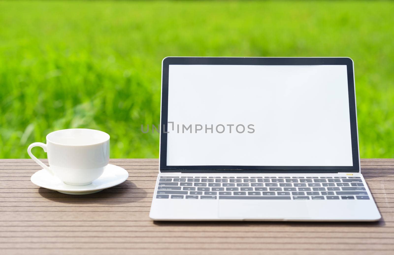 laptop and cofree cup on wood table agent green grass field in countryside