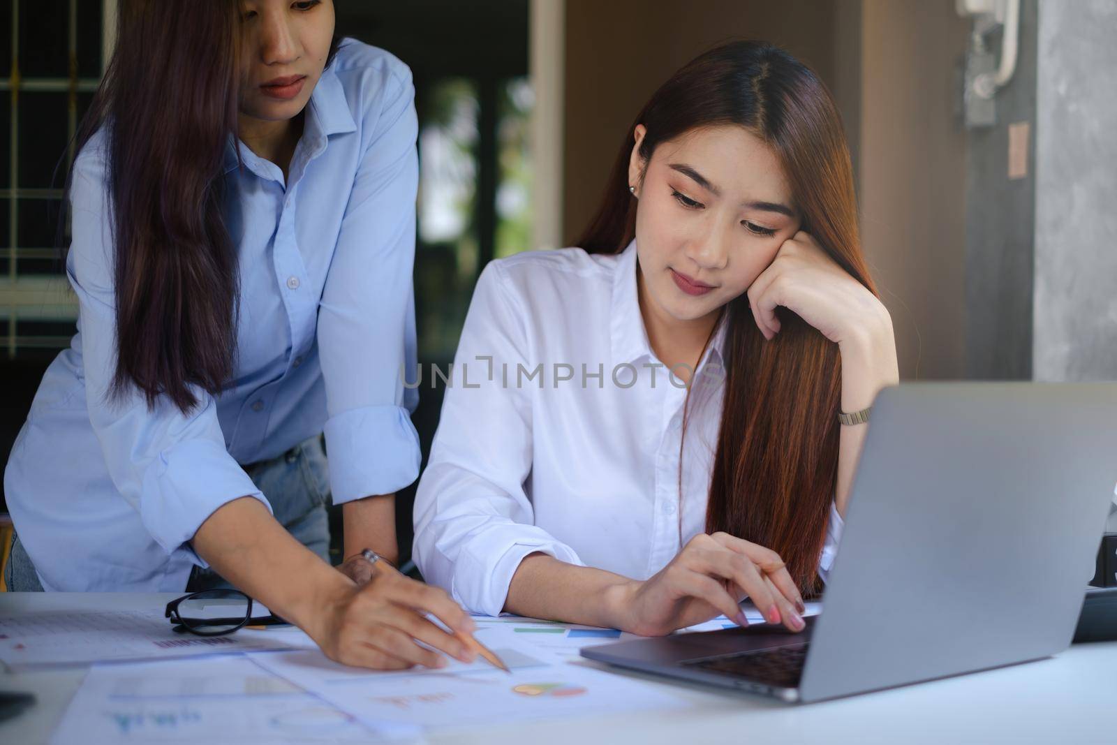 Close-up of a female accountant with partner calculating taxes on a wooden desk in her workplace with numerous documents
