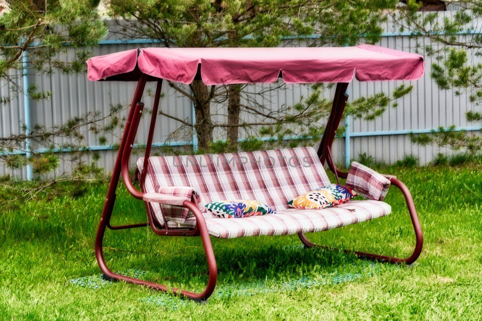 Swing bench with a canopy on a green grassy lawn. Relax in the garden