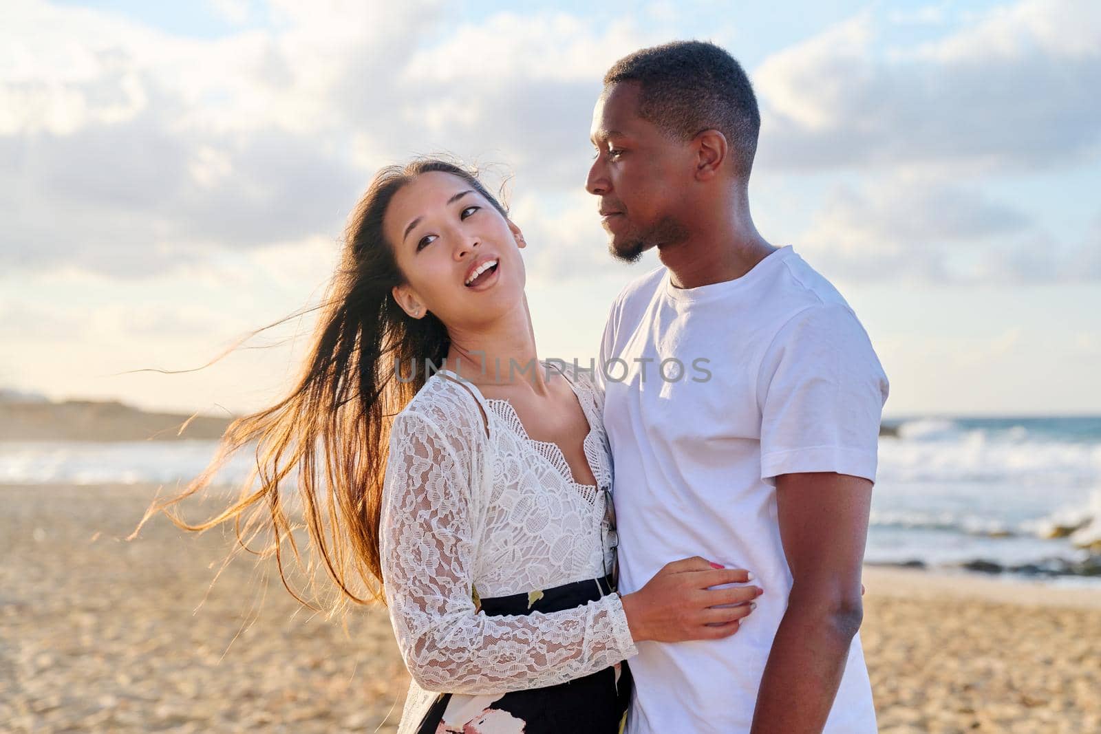 Portrait of happy young beautiful couple on beach. Interracial couple, african american man and asian woman embracing at seaside. People, relationships, dating, vacation, tourism, multi-ethnic family