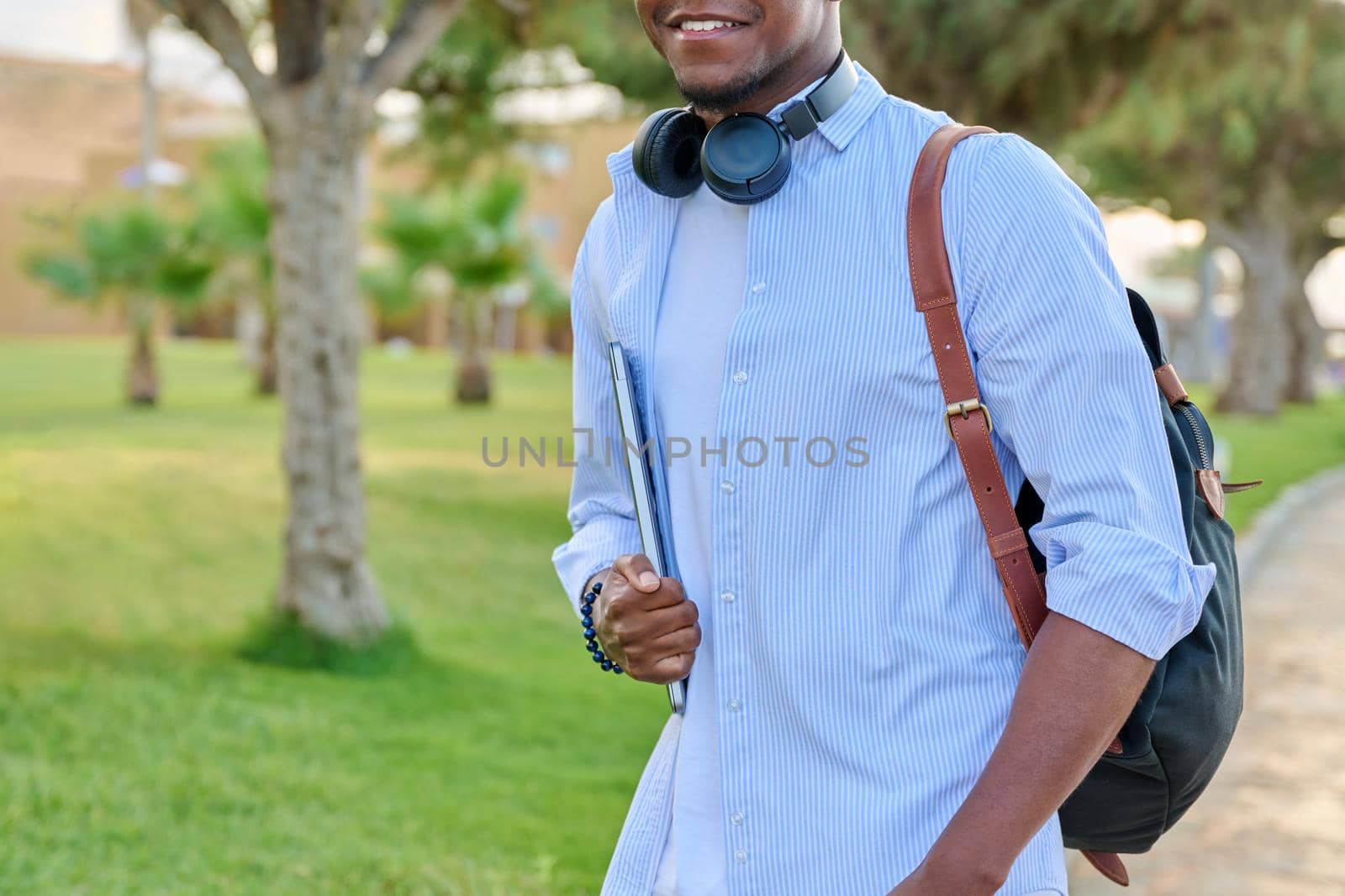 Outdoor portrait of young man with laptop headphones and backpack by VH-studio