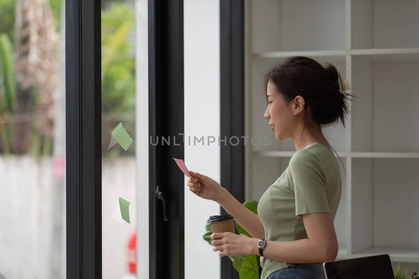 Creative business asian woman reading sticky notes on glass wall at office