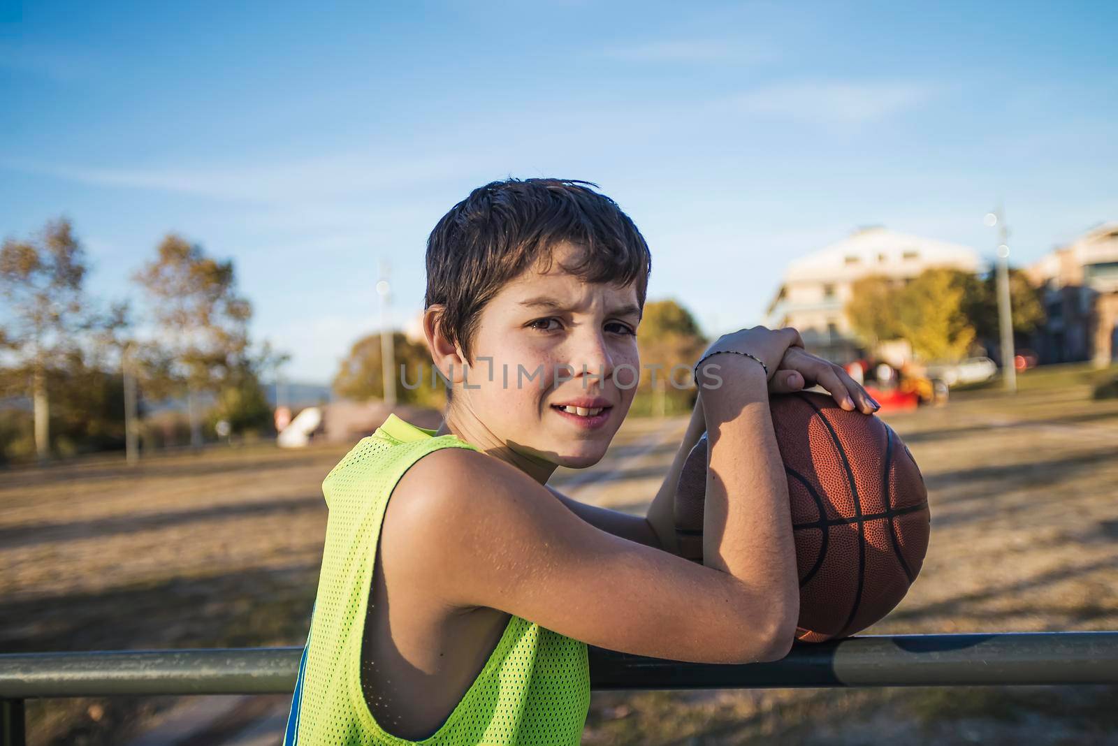 A Young teen male with sleeveless standing on a street basket court while smiling at camera