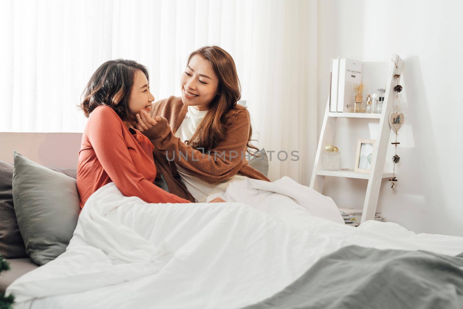 Two happy friends or sisters hugging sitting on a couch in the living room at home by makidotvn