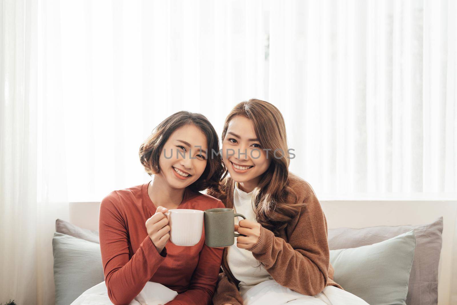 happy friends talking and drinking coffee and tea sitting on a couch at home