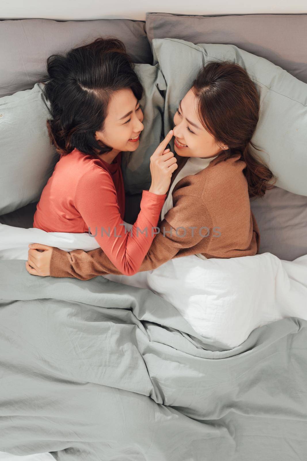 Young lesbian women in love embracing while lying don on bed at home. by makidotvn