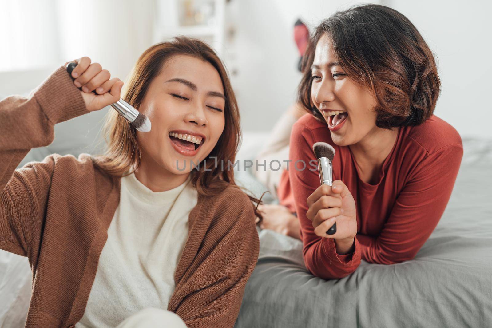 blissful friends fooling around singing while doing makeup in bedroom.