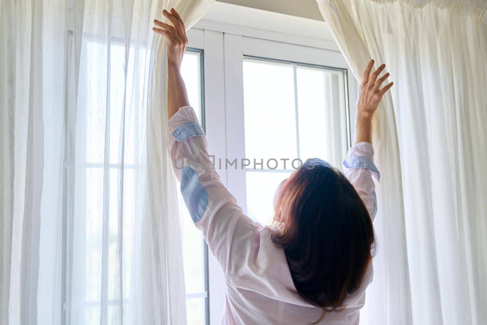 Close-up of woman's hand opening and closing light translucent curtains, back view