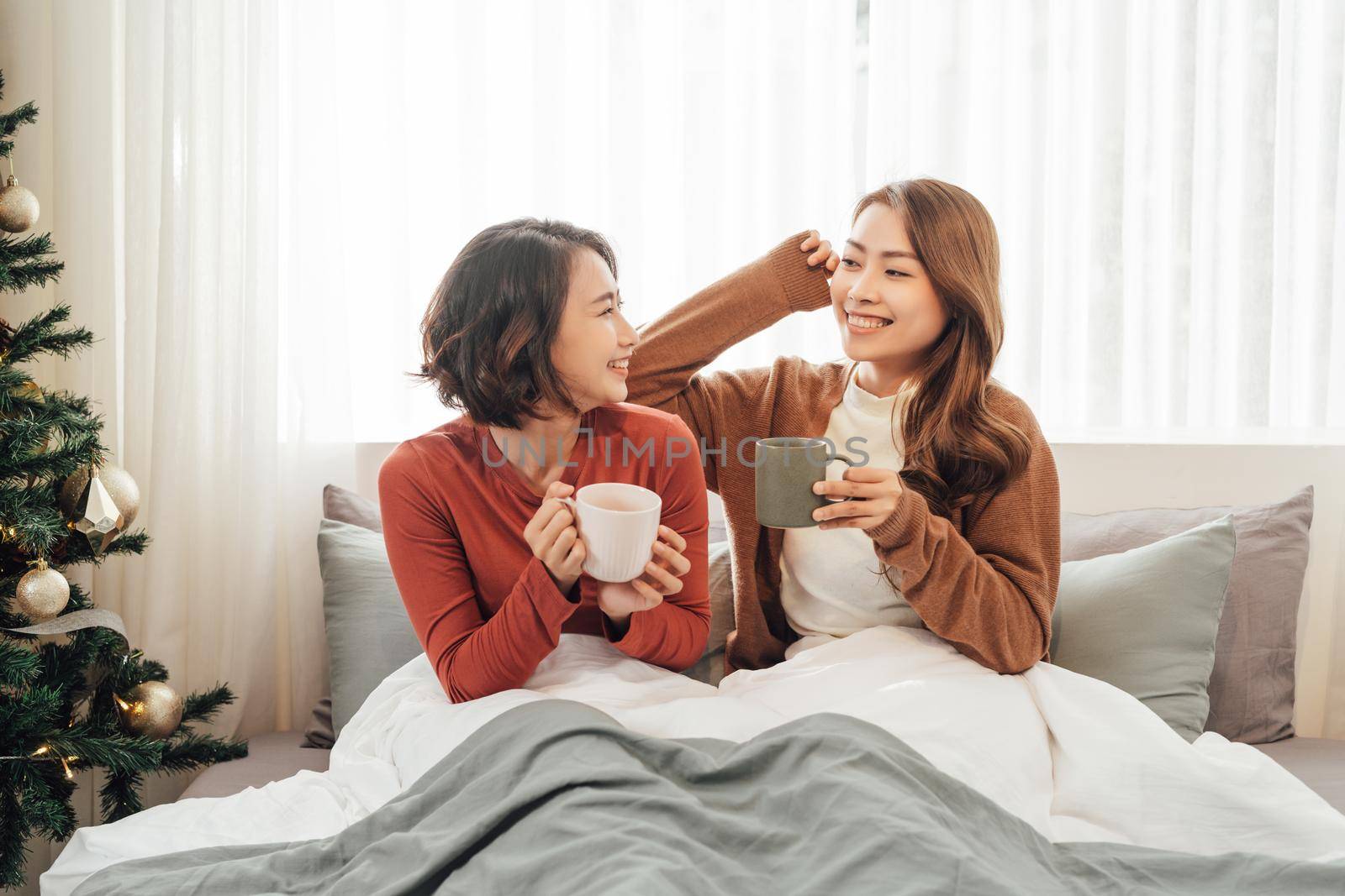 Two female friends relaxing on sofa at home with tea talking together