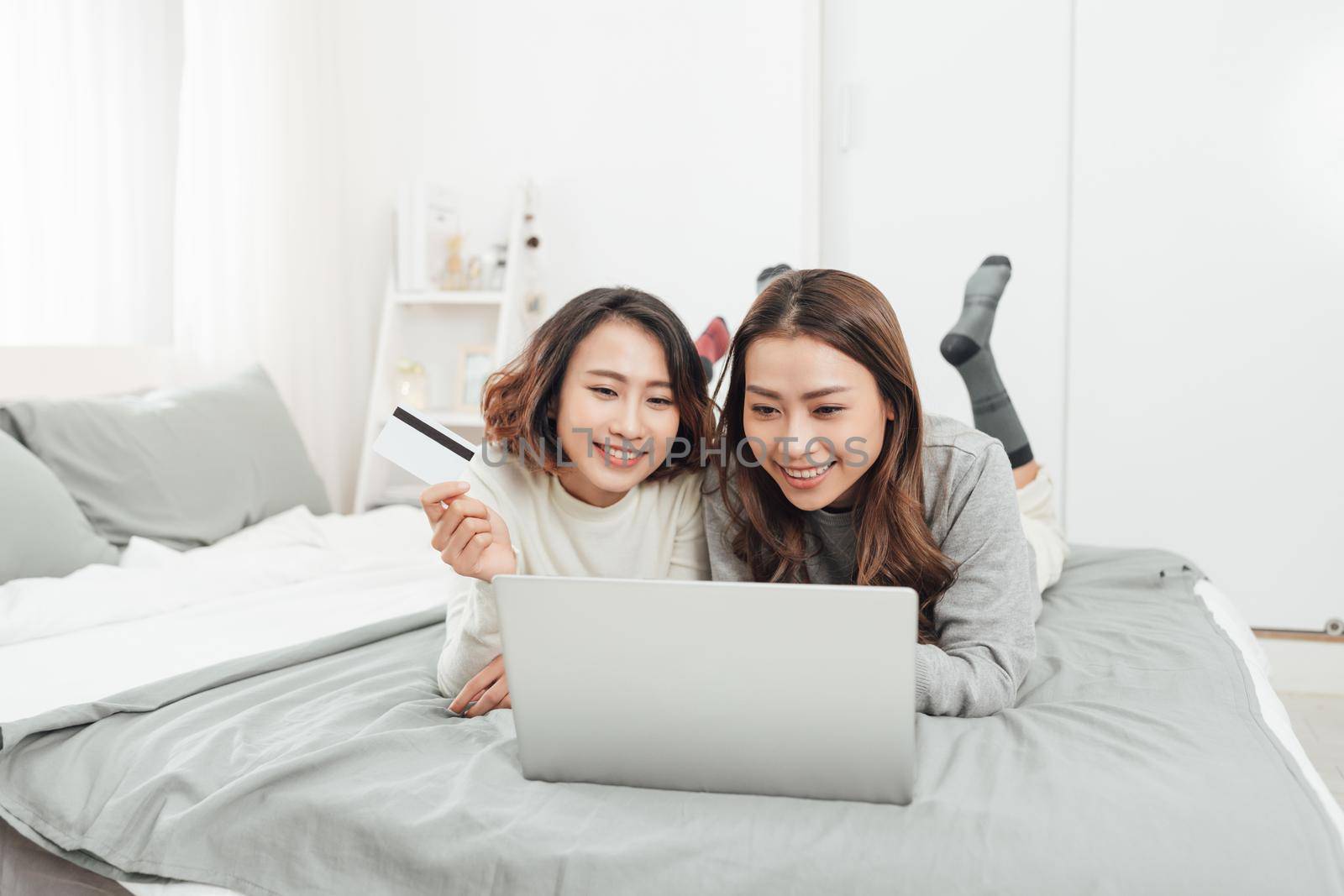 Two happy women shopping online with credit card and laptop at home  by makidotvn