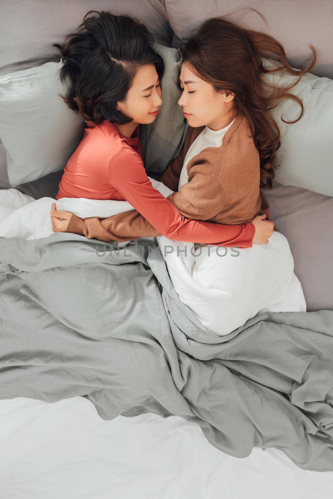 Young lesbian women in love embracing while lying don on bed at home.