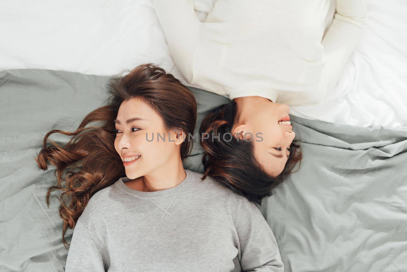 Two smiling women lie on bed