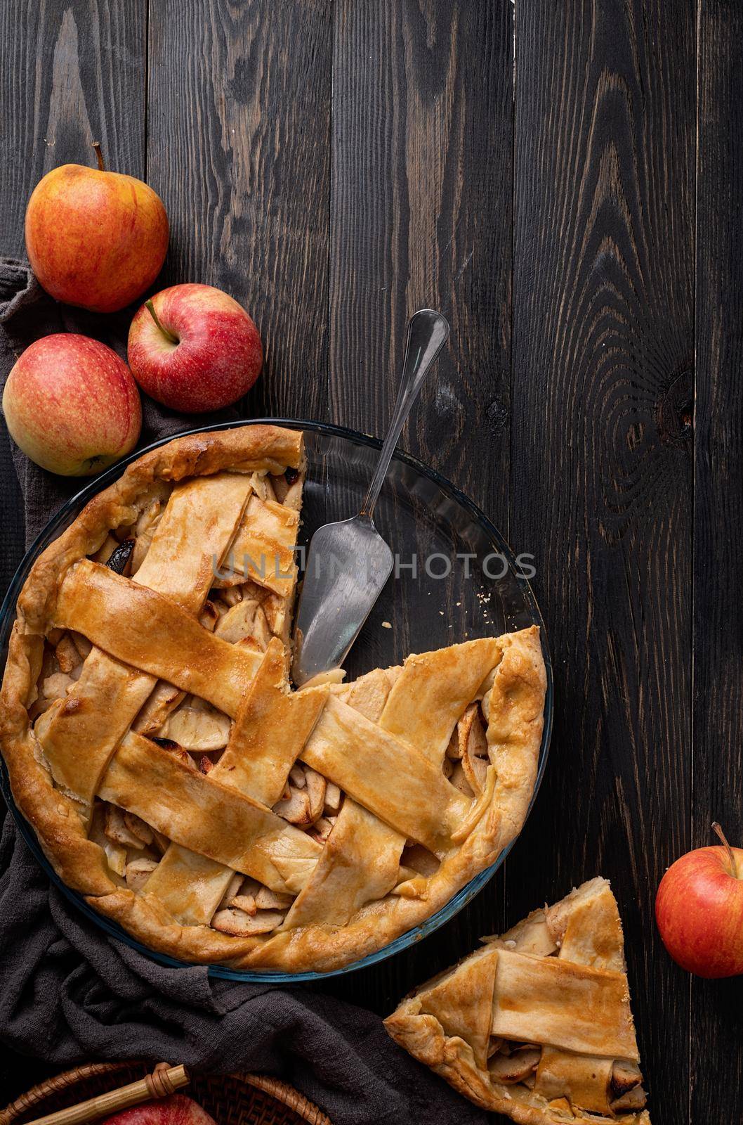 Autumn foods. Top view of homemade apple pie on dark wooden table, decorated with apples, sugar and tablecloth