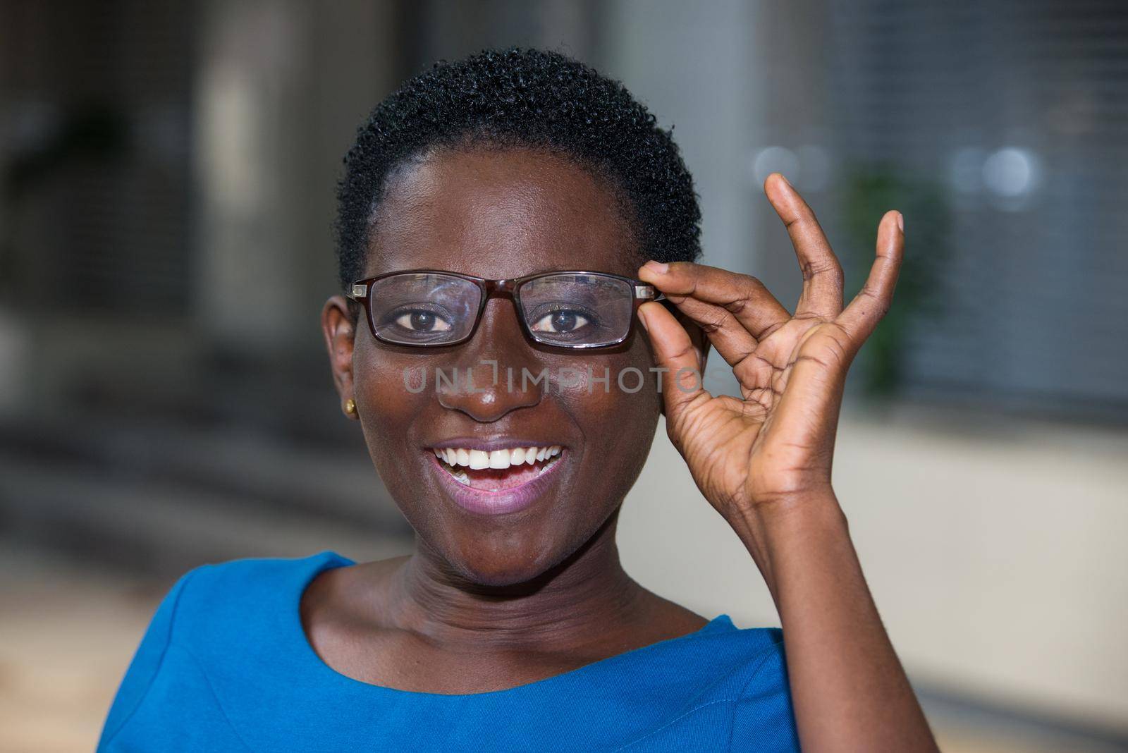 young girl standing in blue camisole eyeglasses looking at camera laughing.