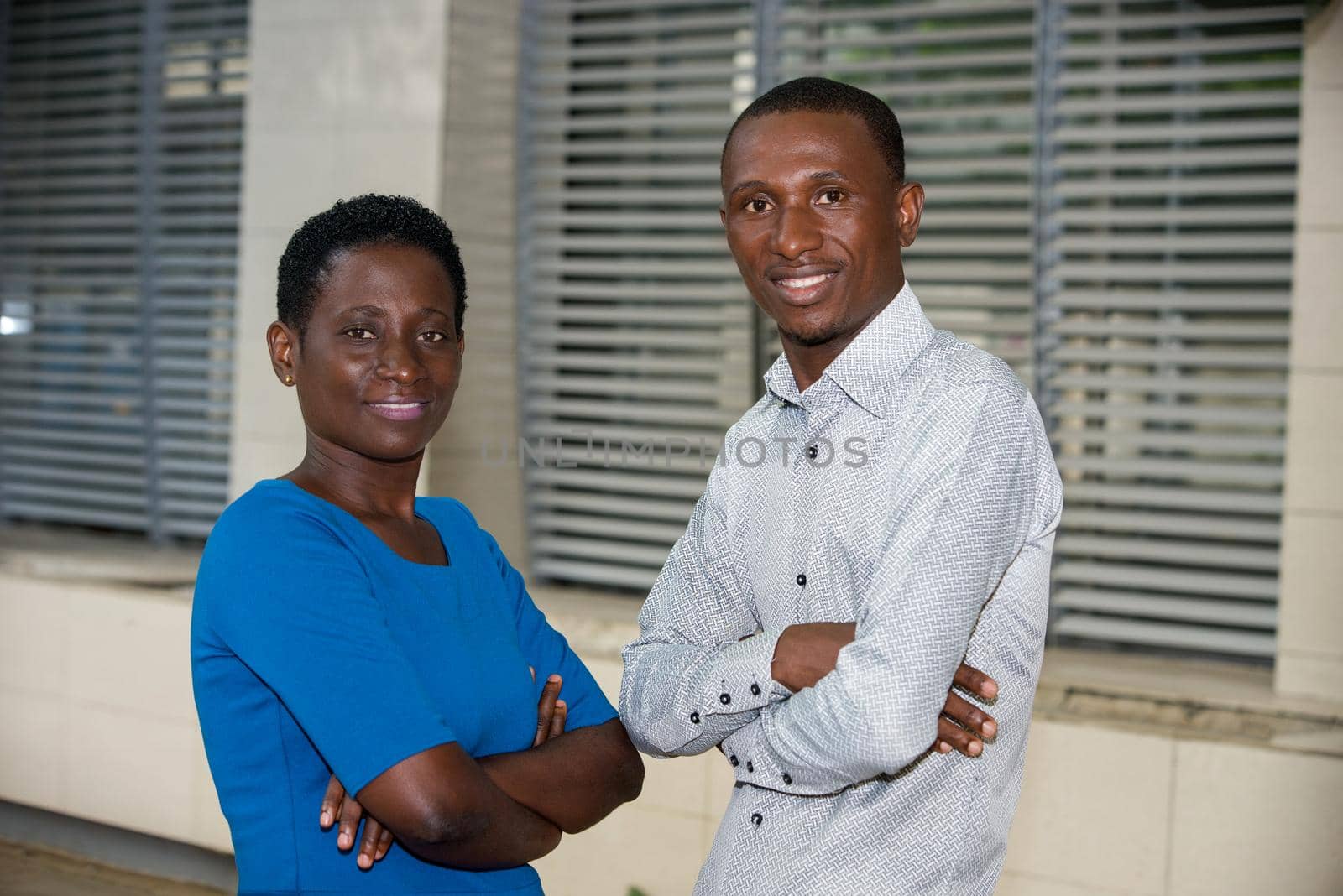 young couple standing crossed arms watching the camera smiling.