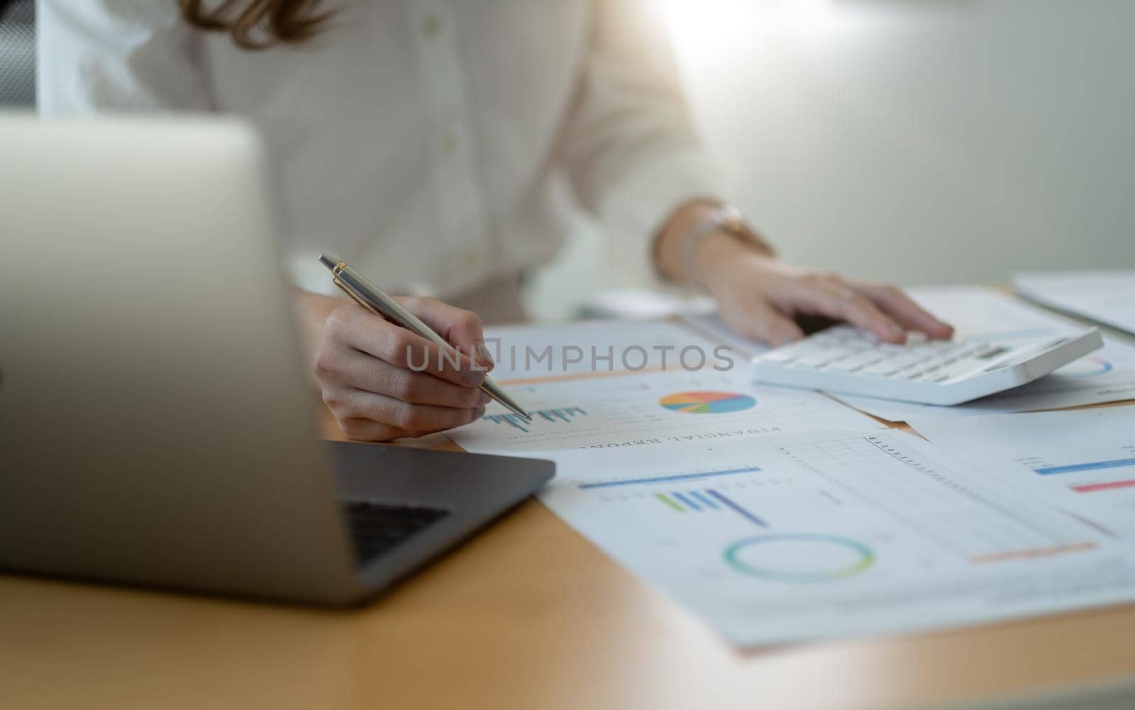 Close up of businesswoman or accountant hand holding pen working on calculator to calculate business data, accountancy document and laptop computer at office, business concept