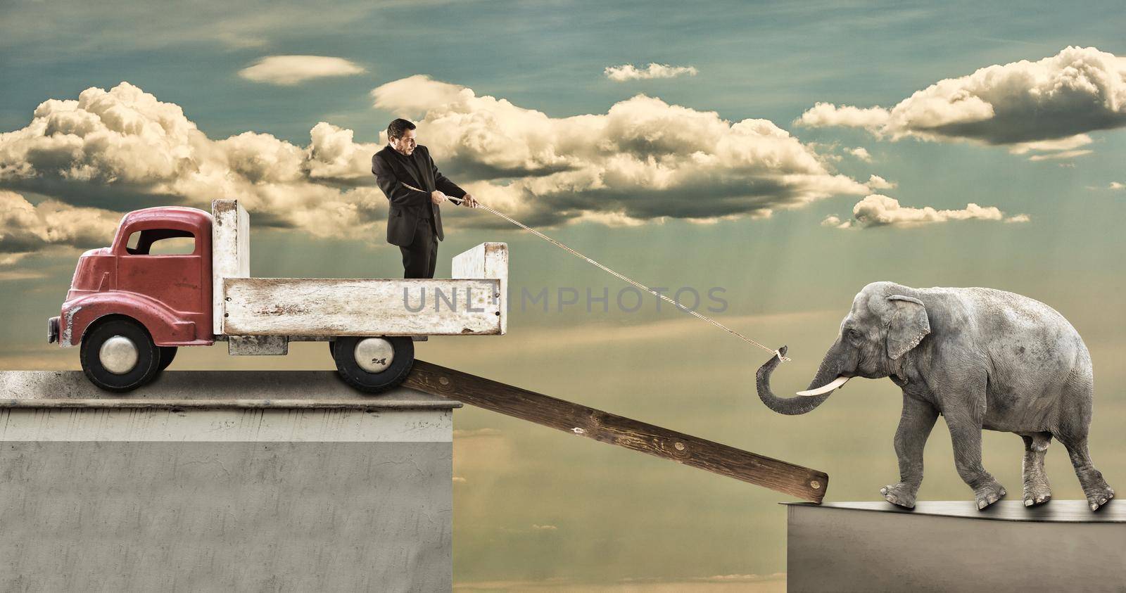 A man using a rope tries to pull an elephant onto the pickup by bepsimage