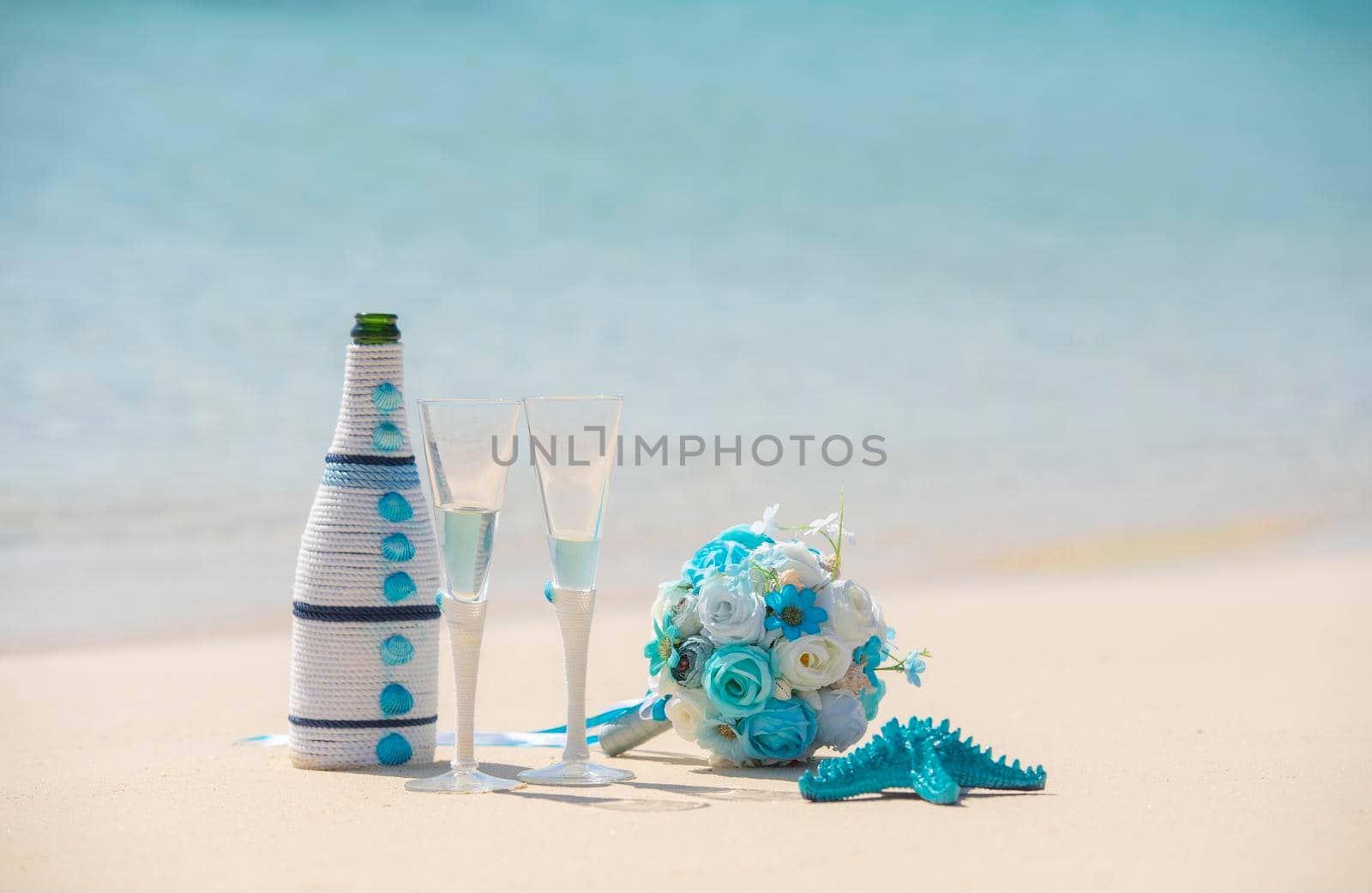 Closeup of champagne wedding romantic decorations still life on tropical island sandy beach paradise with ocean in background