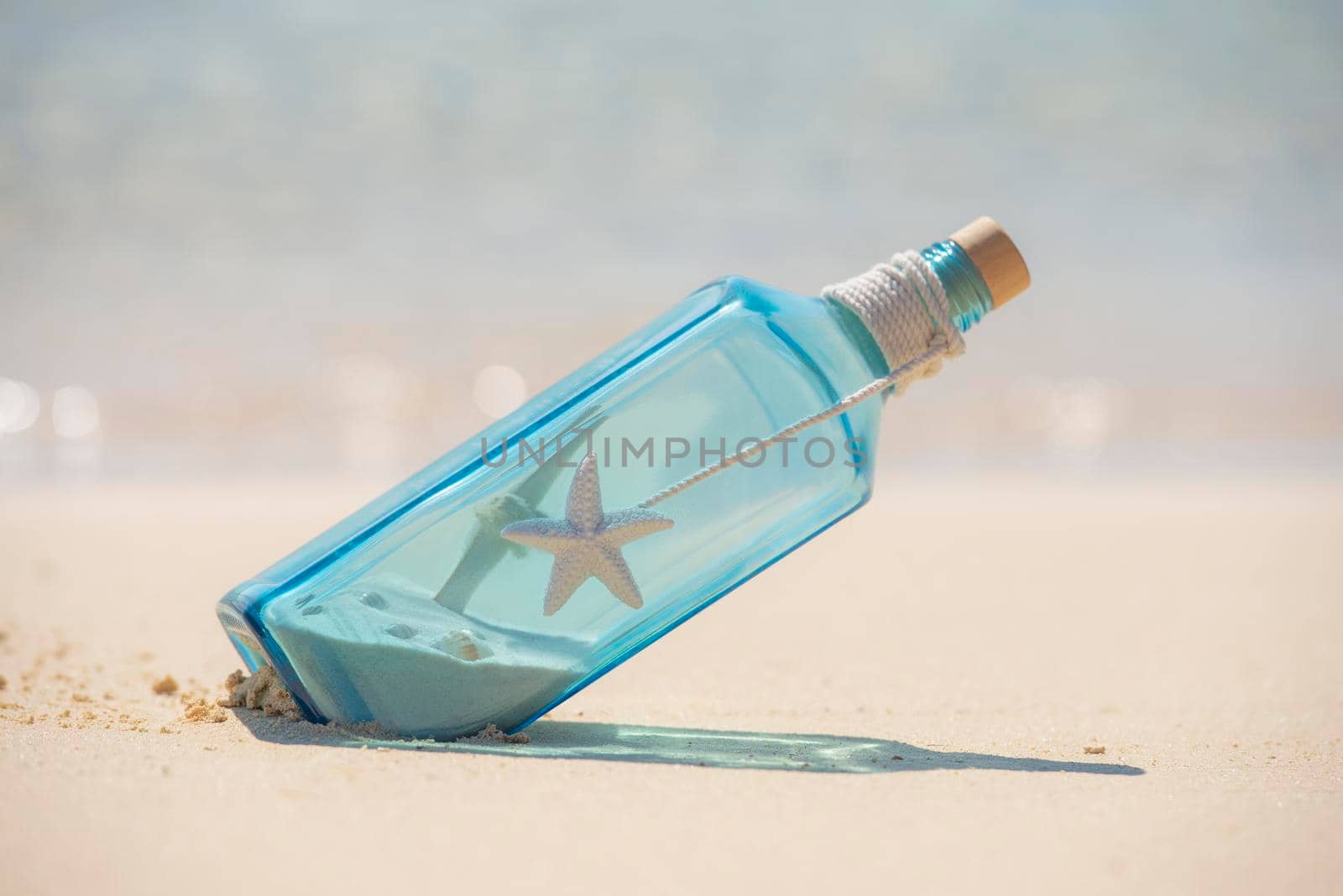 Closeup of blue glass still life on tropical island sandy beach paradise with ocean in background concept message in a bottle