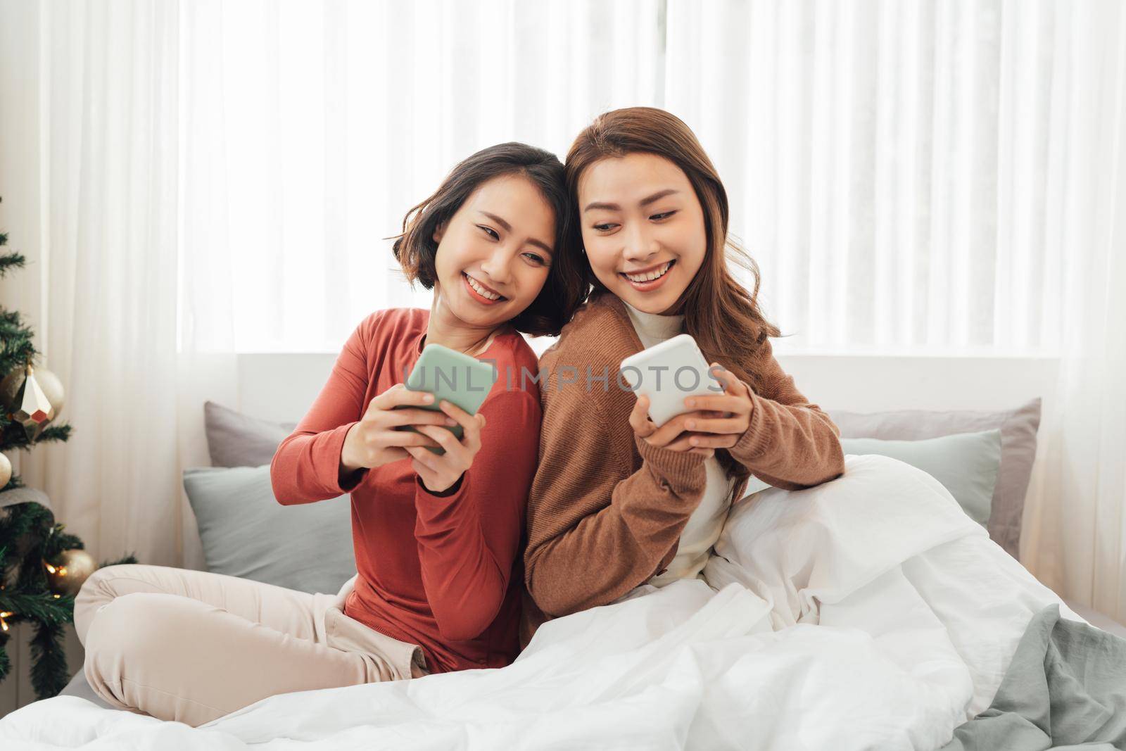 Young happy lesbian lgbtq couple or friends holding smartphone using mobile phone at home